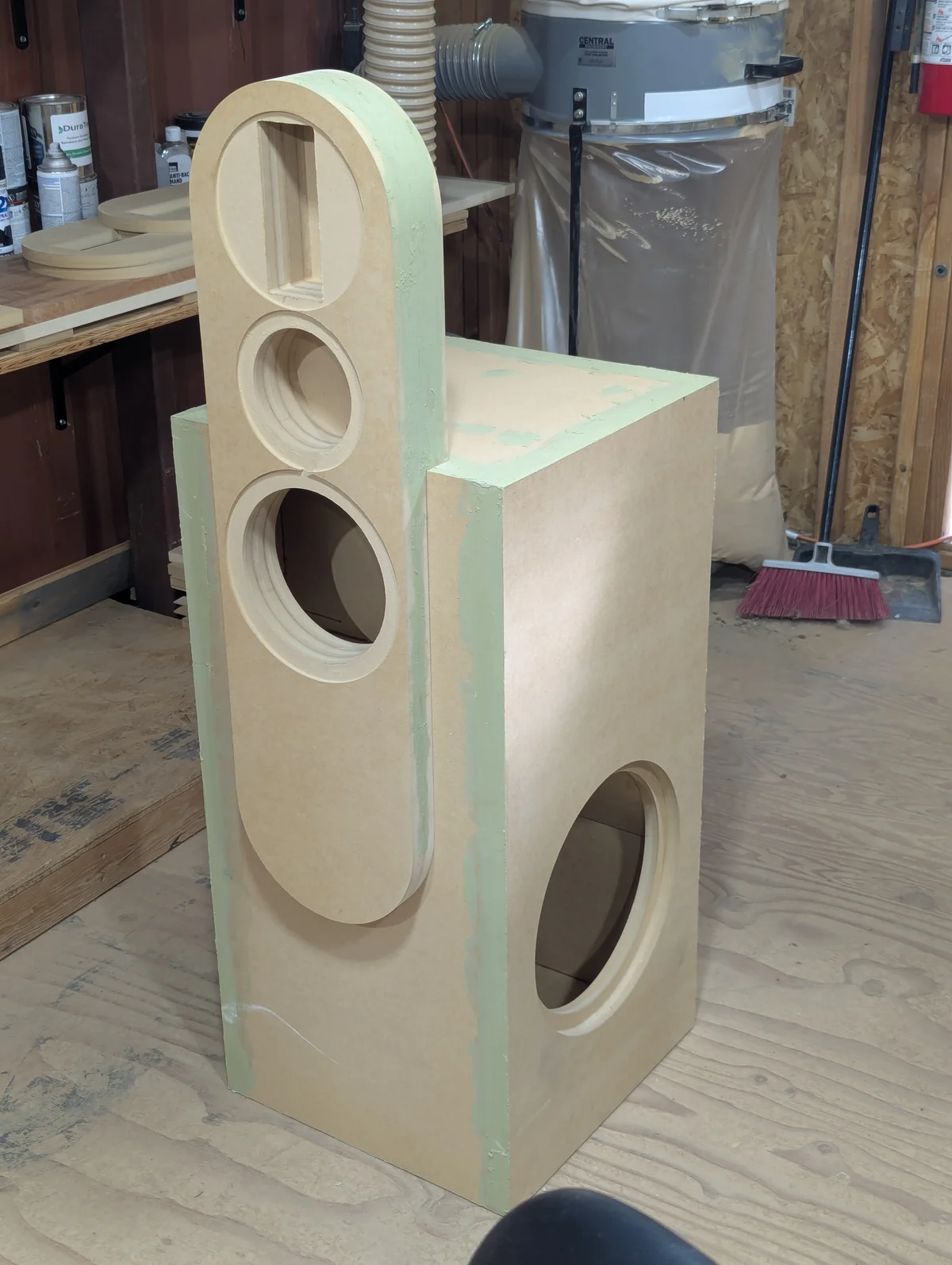 Assembled Wanstreet tower speaker cabinet out of clamps showing pill-shaped upper section with ribbon tweeter slot, dome mid cutout, and 8-inch woofer cutout, with large separate subwoofer base enclosure with single 12-inch driver opening on the front face