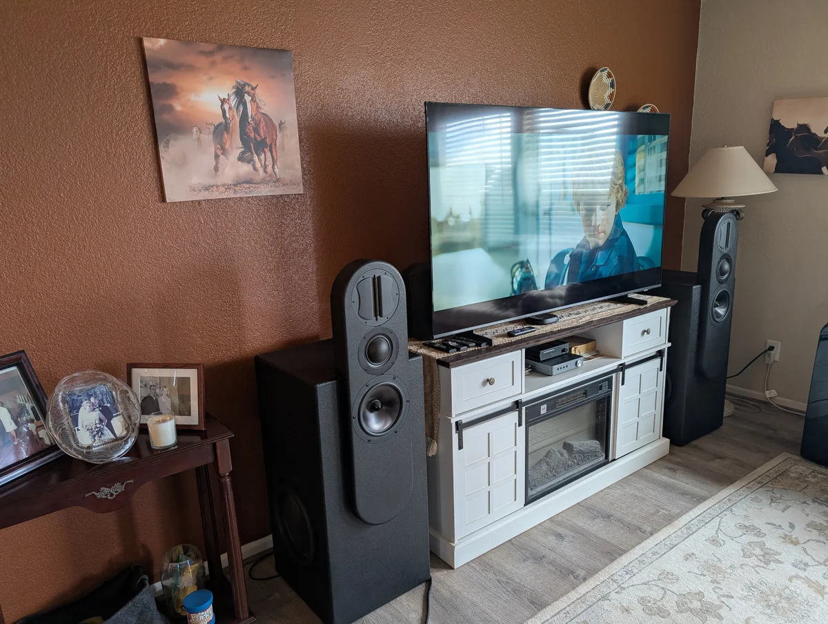 Close angle view of completed Wanderstreet custom WubWub Audio tower speakers installed in Scottsdale living room showing pill-shaped upper section with ribbon tweeter slot and dome mid at eye level with powered subwoofer base and large TV above entertainment console