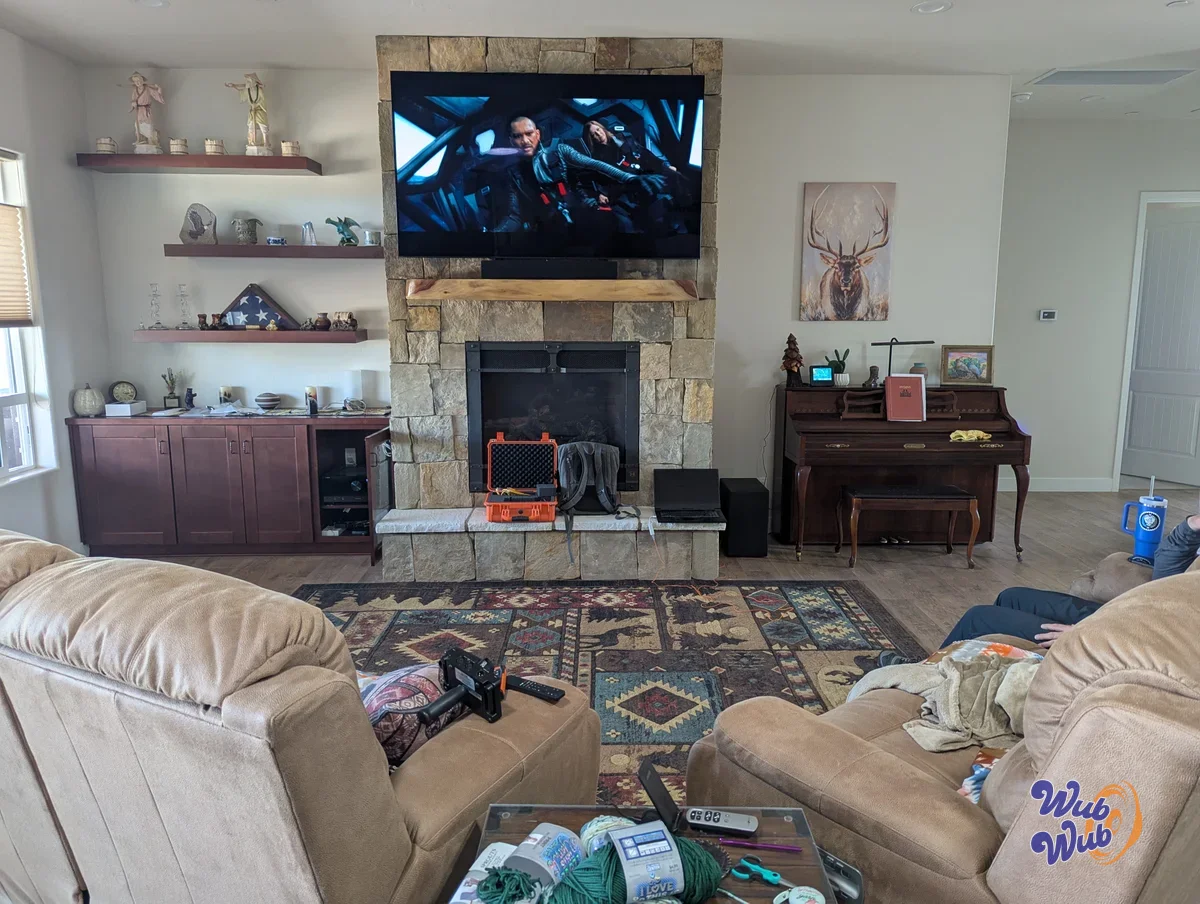 Lafferty Prescott Valley living room with custom center channel speaker already installed on stone fireplace mantle below wall-mounted TV and 500 watt subwoofer tucked invisibly beside upright piano in a low-profile custom home audio installation